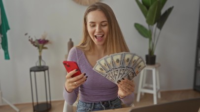 Young woman holding cash with cellphone in other hand