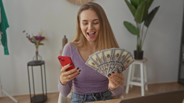 Young woman holding cash with cellphone in other hand