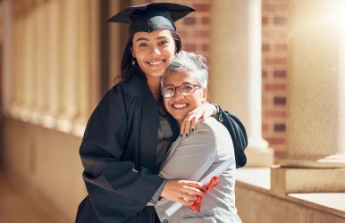 Girl wearing cap and gown embracing her mother