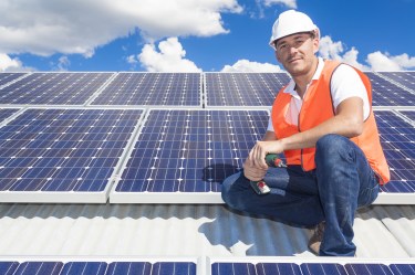 Man in orange vest and white hard hat sits near new solar panels