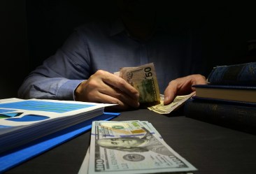 Person counting U.S. dollar bills at a desk with paperwork and books, representing personal loan or cash advance options.