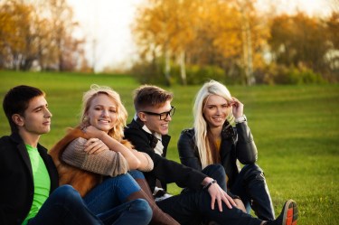 Group of college-aged students sitting together on a grassy campus lawn in the fall